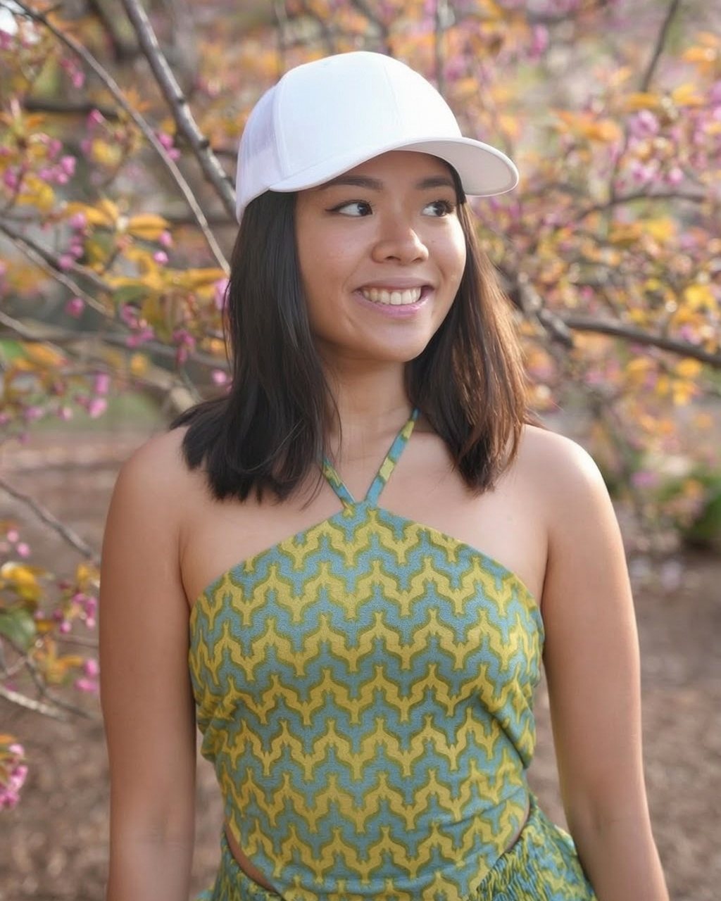 Annika Aguila smiling outdoors under cherry blossoms, wearing a white cap