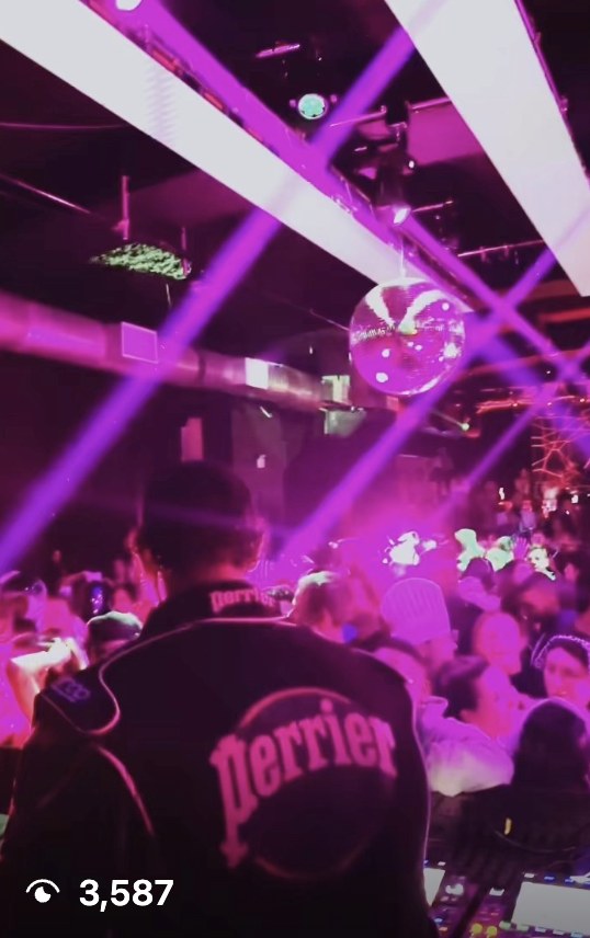 Crowd on the dance floor under a disco ball, DJ wearing a Perrier jacket